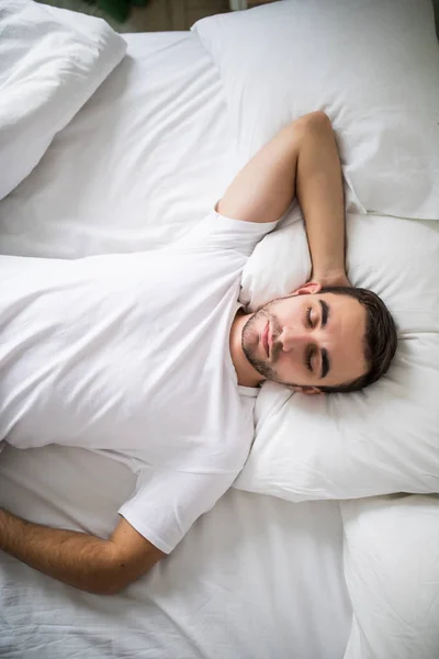 Портрет молодого человека сверху, спящего в белой кровати дома . — стоковое фото