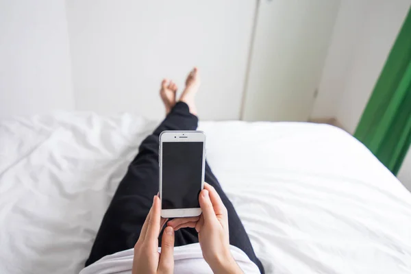 Мужчина в постели дома смотрит на мобильный телефон — стоковое фото