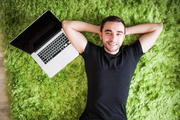 Joven trabajando con un portátil en alfombra de suelo verde — Foto de Stock