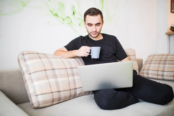 Feliz joven sentado en el sofá y el uso de la computadora portátil — Foto de Stock