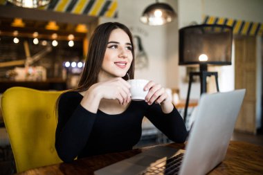 Dizüstü bilgisayar ve içecek kahve kullanan neşeli kadın
