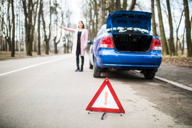 Bir yolda araba sorunu durdurmak ve diğer sürücü yol yardım almak çalışırken bir üçgen koyarak kadın.
