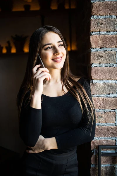 Portrait of the attractive girl speak on mobile phone near window in brick wall background — Stock Photo, Image