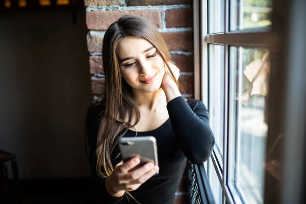 Woman sitting by a window, looking at her cell phone — Stock Photo, Image