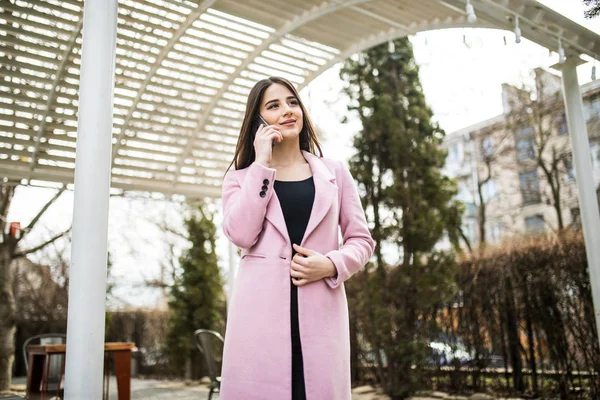 Χαρούμενη γυναίκα που μιλάτε στο τηλέφωνο στο δρόμο φορώντας ένα ροζ παλτό μπουφάν — Φωτογραφία Αρχείου