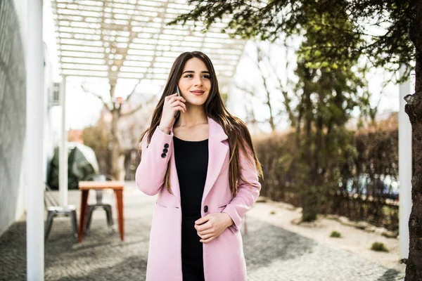 Χαρούμενη γυναίκα που μιλάτε στο τηλέφωνο στο δρόμο φορώντας ένα ροζ παλτό μπουφάν — Φωτογραφία Αρχείου
