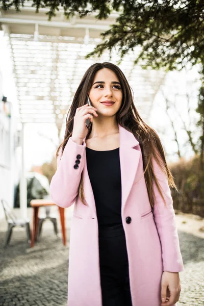 Весела жінка розмовляє по телефону на вулиці в куртці з рожевим пальто — стокове фото