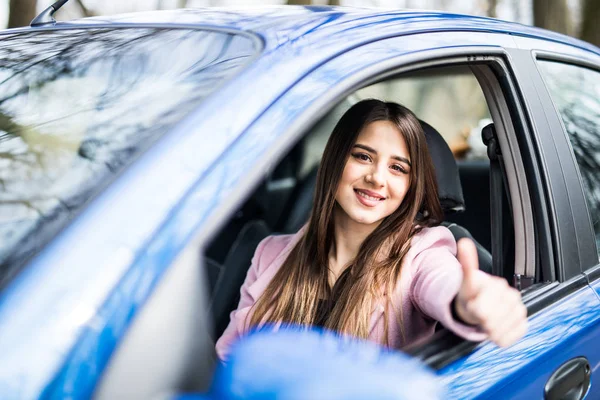 Feliz mujer de negocios con camisa roja oscura conduciendo su coche y mostrando el pulgar hacia arriba. Sonriente dama tomando el volante de su nuevo coche . — Foto de Stock