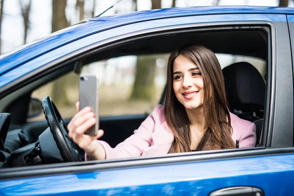Sorrindo jovem mulher tirando foto selfie com câmera de telefone inteligente ao ar livre no carro — Fotografia de Stock