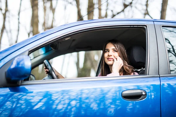 Mujer joven con la mano en el volante usando el teléfono móvil mientras conduce por carretera —  Fotos de Stock