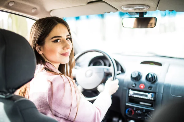 Žena v autě vnitřní udržuje kolo otočila s úsměvem při pohledu na cestující za zadní sedadla. — Stock fotografie