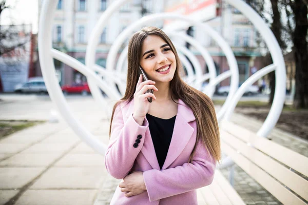 Mujer alegre hablando por teléfono en la calle con una chaqueta rosa —  Fotos de Stock