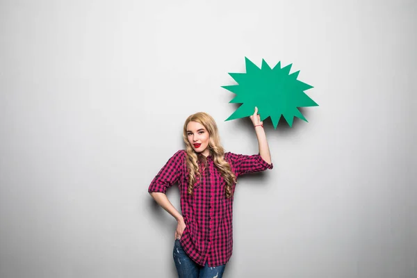 Vrolijke aantrekkelijke jonge vrouw permanent en lege tekstballon houdt over grijze achtergrond — Stockfoto