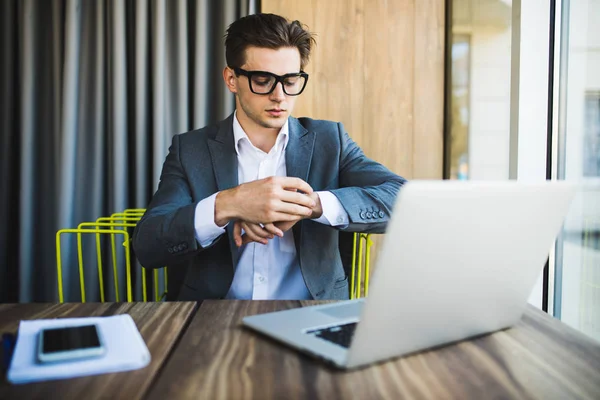 Beau homme d'affaires travaillant avec ordinateur portable dans le bureau et regardant horloge à main à l'heure — Photo