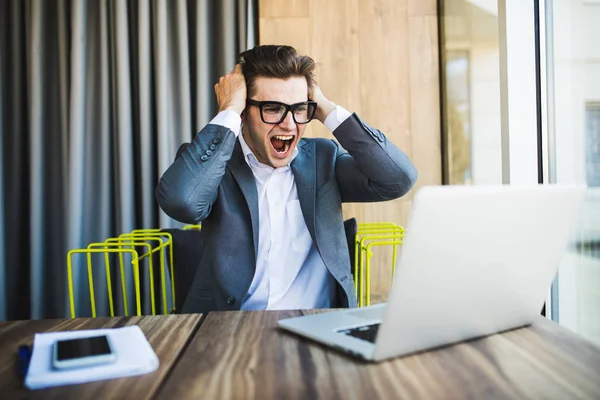 Щасливий бізнесмен в окулярах перемагає з піднятими кулаками і кричить погляд на ноутбук — стокове фото