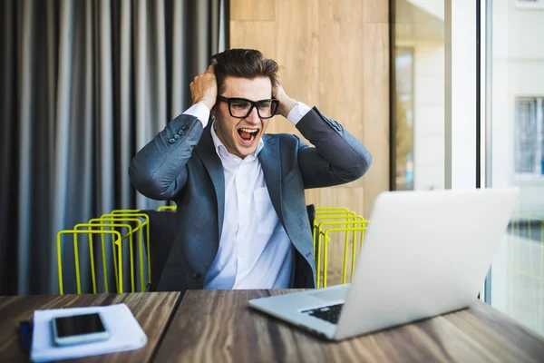 Glad affärsman i glasögon misslyckande med upphöjda nävar på huvudet och skrek titt på laptop — Stockfoto