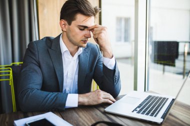 Ofiste dizüstü bilgisayarda çalışan hayal kırıklığına uğramış genç bir iş adamı.