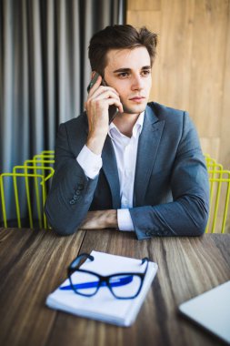 Not kağıdı onun önünde telefonuyla konuşan bir ofiste genç işadamı