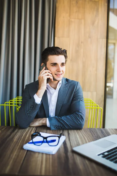 Mladý podnikatel v kanceláři mluvení na svém telefonu s dopisní papír před ním — Stock fotografie