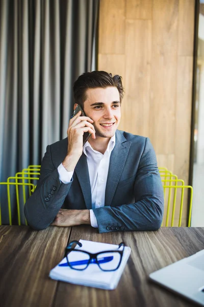 Disfrutando de su trabajo. Feliz joven hombre de negocios hablando en el teléfono móvil en el cuaderno delantero mientras está sentado en su lugar de trabajo — Foto de Stock