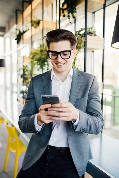 Portrét šťastné usmívající se podnikatel v brýlí pomocí smartphone, zatímco sedí v kanceláři — Stock fotografie