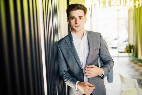 高価なスーツに身を包んだビジネスマンは彼の会社の廊下で立っています。若い男性マネージャーが近代的なオフィスにポーズをとってください。 — ストック写真