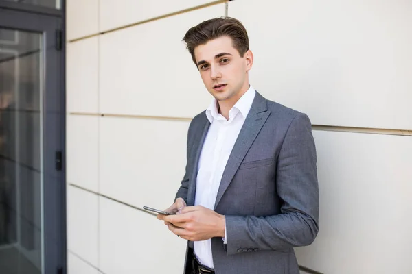 Městské profesionální mladík pomocí chytrého telefonu v kancelářské budově uvnitř. Podnikatel drží mobilní smartphone pomocí aplikace SMS sms zprávy nošení saka. — Stock fotografie