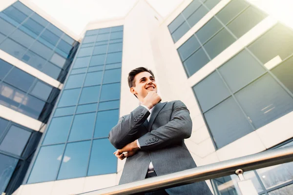 Jeune homme d'affaires attrayant avec les mains sur le menton devant un immeuble de bureaux moderne par une belle journée ensoleillée . — Photo