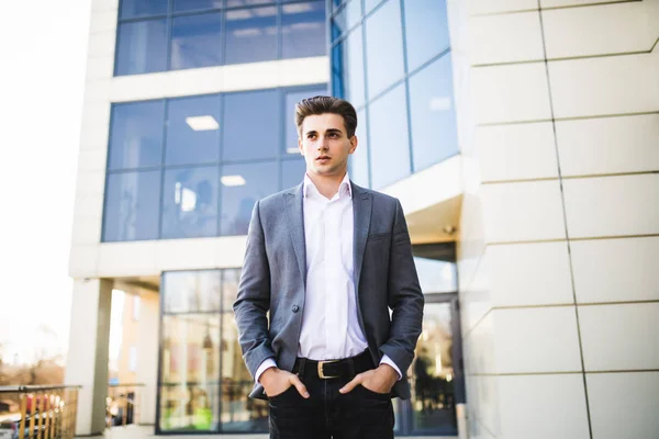 Elegante bonito jovem empresário enquanto caminha na frente do prédio de escritórios — Fotografia de Stock