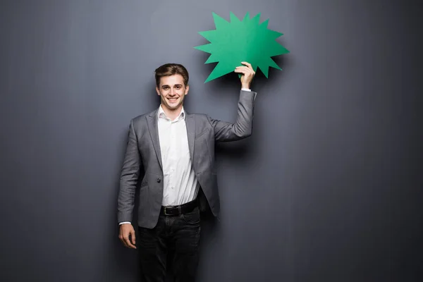 Молодий красивий чоловік тримає зелену бульбашку для тексту, ізольований на сірому фоні — стокове фото