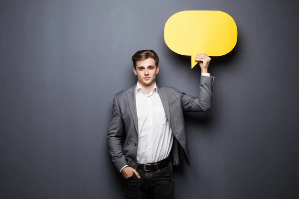 Jovem homem bonito segurando uma bolha amarela para o texto, isolado em um fundo cinza — Fotografia de Stock