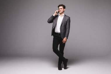 Gri bir arka plan üzerinde izole cep telefonuyla konuşan tam yükseklikte işadamı