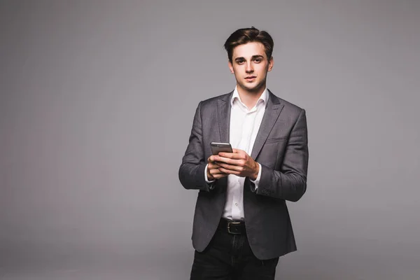 Retrato de un joven hombre de negocios enviando un mensaje con un teléfono sobre un fondo gris — Foto de Stock