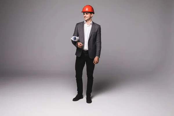 Bonito arquiteto jovem em capacete de proteção está estudando esboço em fundo cinza — Fotografia de Stock