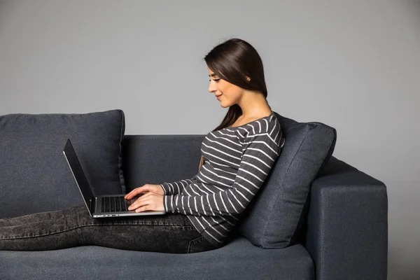 Portrait latéral d'une belle jeune femme assise sur un canapé et utilisant un ordinateur portable à la maison — Photo