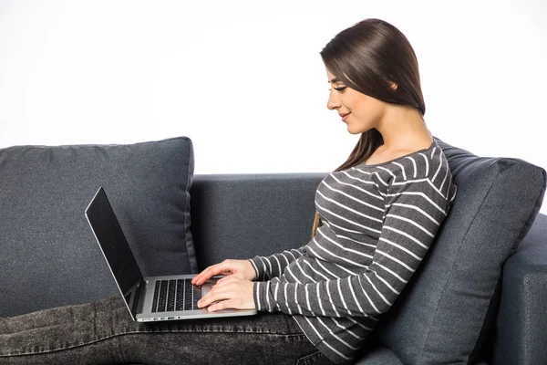 Portrait latéral d'une belle jeune femme assise sur un canapé et utilisant un ordinateur portable à la maison — Photo