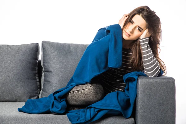 Fiatal nő ül egy kanapén, tartja a fejét, miután egy erős fejfájás fedett takaró — Stock Fotó