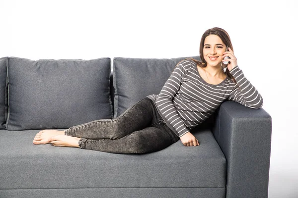 Happy young woman talking cell phone while lying on sofa on white — Stock Photo, Image