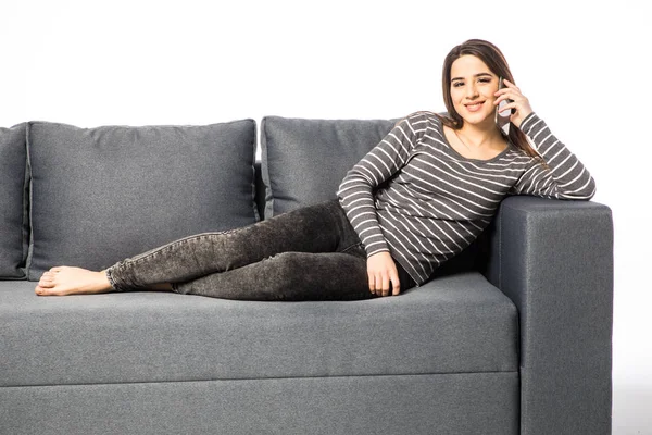 Happy young woman talking cell phone while lying on sofa on white — Stock Photo, Image