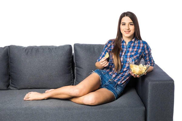 若い魅力的な女性のソファーに座っていると白い背景の上のチップを食べる — ストック写真