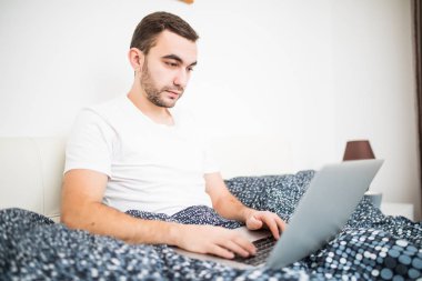 Genç adam gülümseyen evde yatakta yatarken dizüstü bilgisayar ile çalışma
