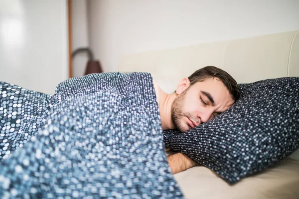 Молодой красивый мужчина спит комфортно в постели дома — стоковое фото