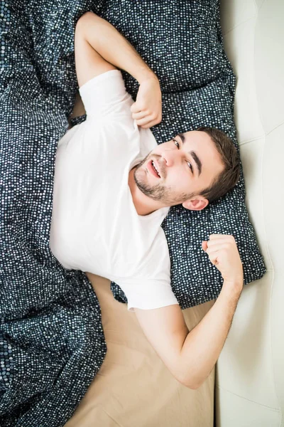 Молодой красивый счастливый мужчина просыпается на кровати дома, вид сверху — стоковое фото