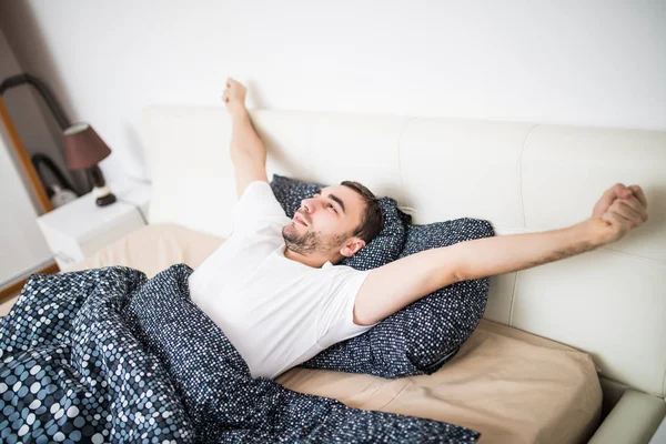 Зияющий и растягивающий мужчина просыпается в постели дома — стоковое фото