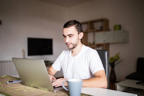 Retrato de un joven usando un ordenador portátil mientras desayunaba por la mañana — Foto de Stock