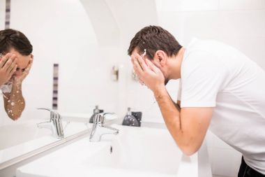 Parlak beyaz adam yüzünü evde banyoda su püskürtme