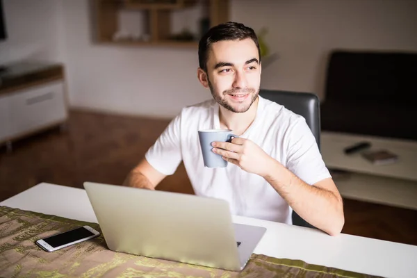 Joven sentado en la mesa con portátil y taza de café en la mañana — Foto de Stock