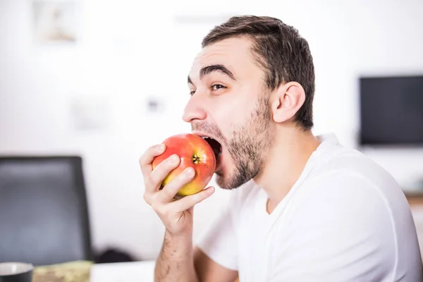 Retrato de um homem comendo uma maçã na cozinha — Fotografia de Stock