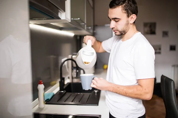 Adam mutfakta bir fincan sıcak kahve cam aranjman dökme. Sabahları kahvaltı — Stok fotoğraf