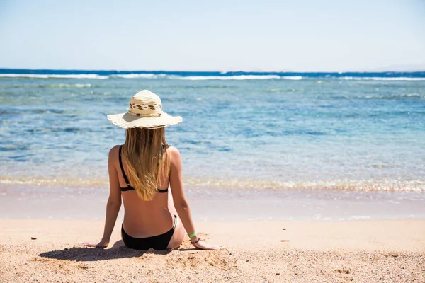 Mulher na praia sentada na areia olhando para o oceano desfrutando de sol e férias de viagem de verão fuga de férias. Menina de biquíni relaxante sob o céu azul . — Fotografia de Stock